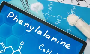 Tablet z napisem fenyloalanina i wzorem chemicznym. Obok probówka z białym proszkiem.