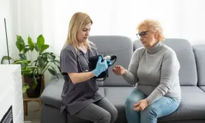 Pielęgniarka wykonuje wizyty domowe NFZ, mierząc ciśnienie starszej pacjentce.