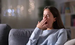 Kobieta zamyka oczy i ziewa, zakrywając usta dłonią. Jej twarz wyraża zmęczenie, być może objaw hipersomnii.