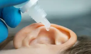 Kropla leku do ucha, by ulżyć przy zatkanym uchu i szumie. Ręka w niebieskiej rękawiczce trzyma pipetę.