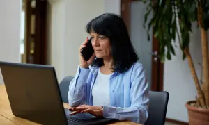 Kobieta rozmawia przez telefon, sprawdzając jak sprawdzić status skierowania do sanatorium NFZ na laptopie.