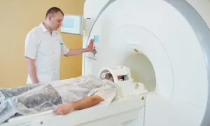 Pacjent leży w aparacie do rezonansu magnetycznego. Technik nadzoruje badanie, przygotowując rejestrację.