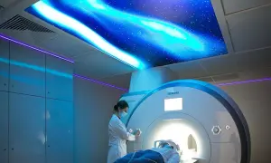 Pacjent leży w aparacie MRI, a technik przygotowuje badanie. Sufit ozdobiony jest motywem kosmicznym, co może pomóc w odpowiedzi na pytanie, ile trwa rezonans głowy.