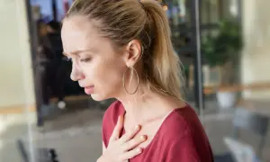 Kobieta z bólem w klatce piersiowej, trzymająca się za serce, doświadcza najgorszych objawów refluksu.