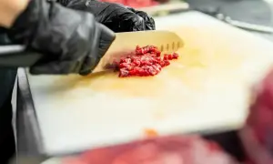 Ręce w czarnych rękawiczkach siekają mięso na desce. Uważaj na listeriozę, dbaj o higienę podczas przygotowywania jedzenia.
