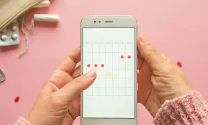 Dłoń trzyma smartfon z kalendarzem cyklu. Czy ginekolog może zbadać podczas okresu? Na ekranie zaznaczone dni miesiączki.