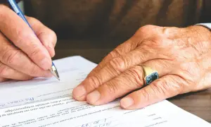 Dłoń z sygnetem podpisuje dokument. Ważne jest skierowanie na badania, aby uzyskać właściwą diagnozę.