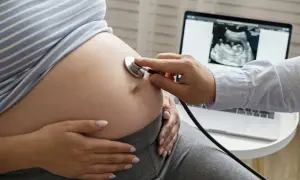 Lekarz osłuchuje brzuch ciężarnej, na ekranie laptopa zdjęcie USG. To obraz prowadzenia ciąży na NFZ.