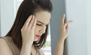 Kobieta z ręką na skroni, cierpiąca na zawroty głowy, które mogą być objawami problemów z błędnikiem.