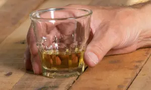 Dłoń trzyma kieliszek z bursztynowym płynem. Czy alkohol podnosi ciśnienie? To pytanie nurtuje wielu.