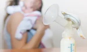 Laktator z butelką mleka, w tle mama z dzieckiem. Nawał pokarmu w której dobie to wyzwanie, ale dzięki niemu maluch ma co jeść.