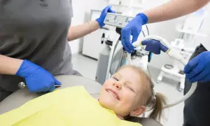 Uśmiechnięta dziewczynka na fotelu dentystycznym, stomatolog przygotowuje sprzęt.