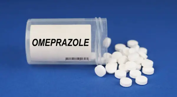 Białe tabletki z napisem OMEPRAZOLE rozsypane z pojemnika. Bioprazol Max to lek, który może pomóc w problemach z żołądkiem.