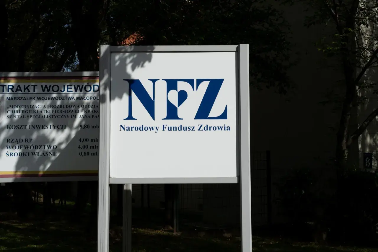 Tablica z logo NFZ i napisem Narodowy Fundusz Zdrowia. Obok tablica z informacjami o inwestycjach, jak sprawdzić oddział NFZ.