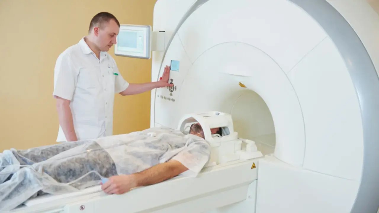 Pacjent leży w aparacie do rezonansu magnetycznego. Technik nadzoruje badanie, przygotowując rejestrację.