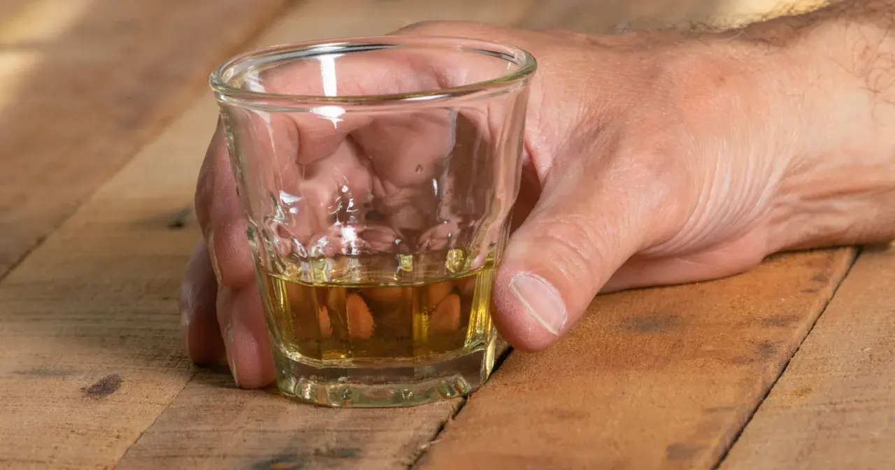 Dłoń trzyma kieliszek z bursztynowym płynem. Czy alkohol podnosi ciśnienie? To pytanie nurtuje wielu.