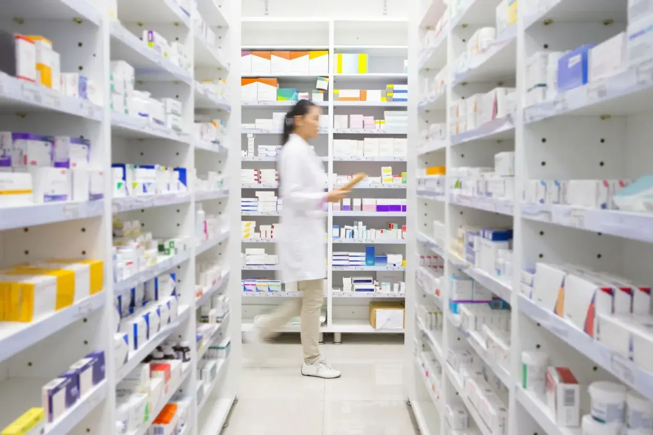 Farmaceutka w białym fartuchu przegląda półki z lekami, szukając informacji o ketrel skutki uboczne.