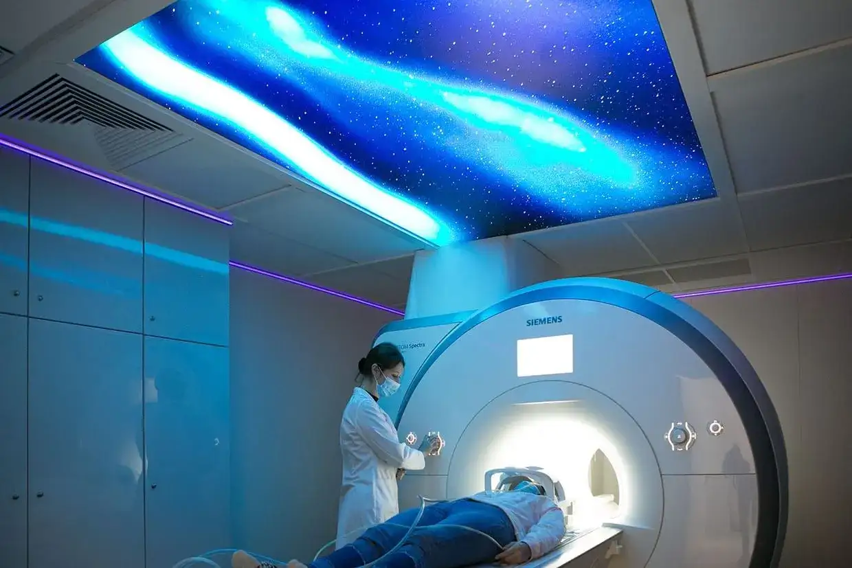 Pacjent leży w aparacie MRI, a technik przygotowuje badanie. Sufit ozdobiony jest motywem kosmicznym, co może pomóc w odpowiedzi na pytanie, ile trwa rezonans głowy.