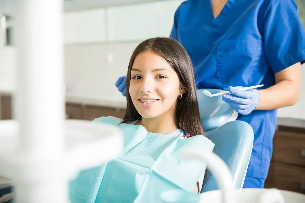 Uśmiechnięta dziewczynka z aparatem ortodontycznym na wizycie u dentysty. Stomatologia dziecięca NFZ to troska o zdrowe zęby najmłodszych.
