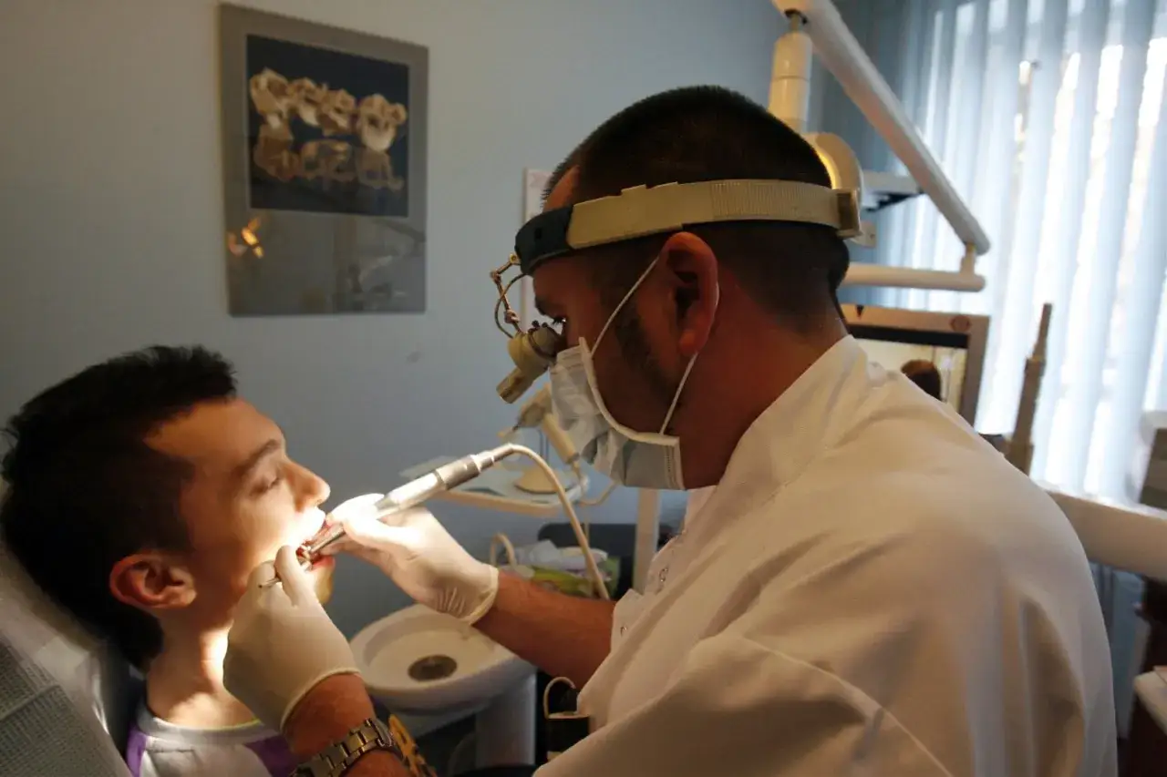 Ostry dyżur stomatologiczny Warszawa NFZ Lindleya: dentysta w masce i okularach z lupą leczy zęby pacjenta.