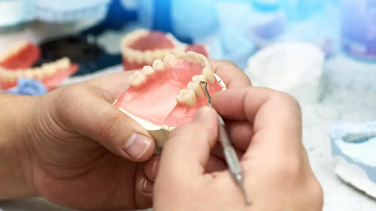 Dłoń technika dentystycznego dopracowuje protezy akronowe na NFZ.