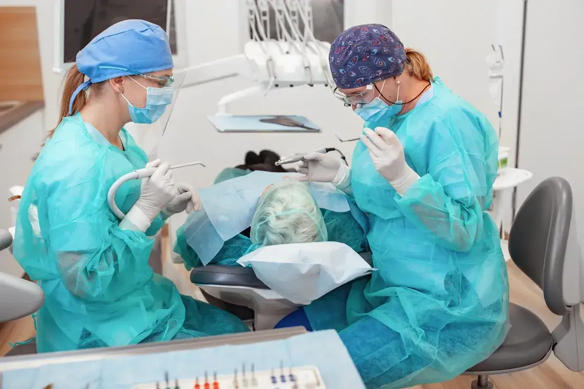 Ostry dyżur stomatologiczny Warszawa NFZ Lindleya: dwie lekarki w maseczkach i fartuchach pracują przy pacjentce w gabinecie.