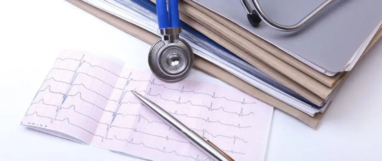 Stetoskop i długopis na EKG, stos dokumentów w tle. Dowiedz się, jak zmienić przychodnię NFZ.