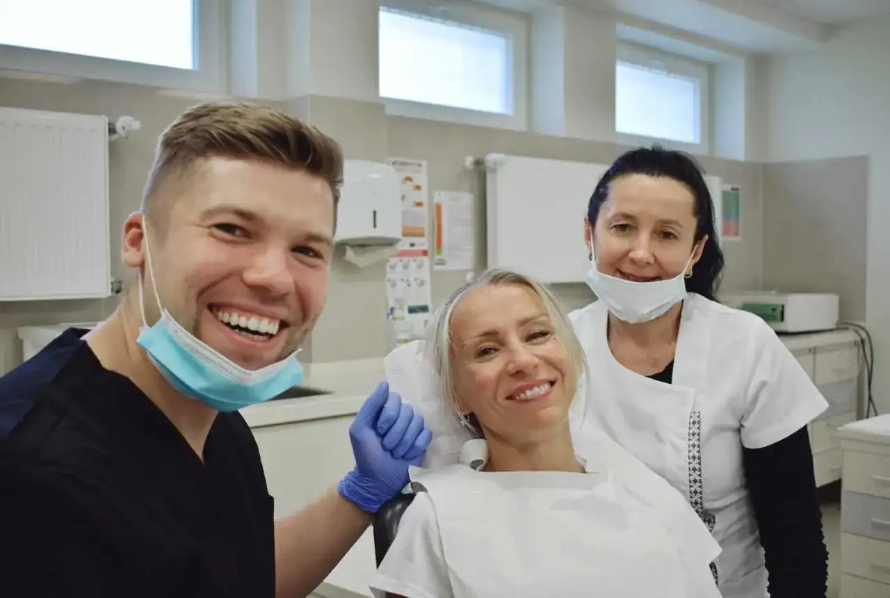 Uśmiechnięty dentysta i asystentka podczas wizyty pacjentki. Stomatologia Lindleya NFZ oferuje profesjonalną opiekę.