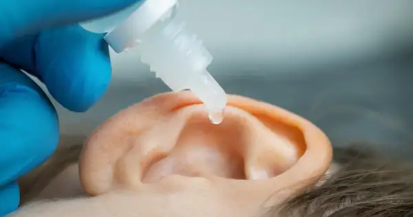 Kropla leku do ucha, by ulżyć przy zatkanym uchu i szumie. Ręka w niebieskiej rękawiczce trzyma pipetę.