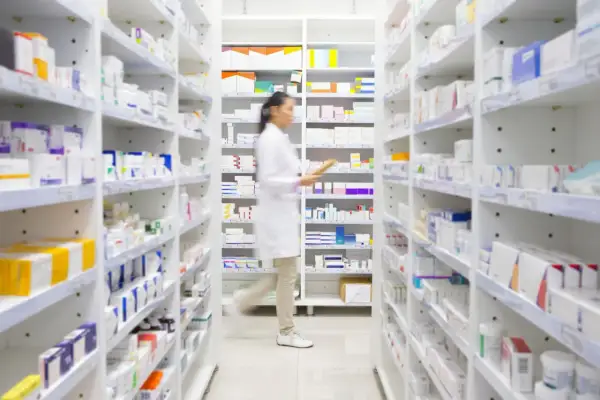 Farmaceutka w białym fartuchu przegląda półki z lekami, szukając informacji o ketrel skutki uboczne.
